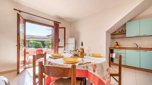 Un comedor con una mesa dispuesta para cuatro personas, una cocina con gabinetes color turquesa y vistas a un patio con baldosas.