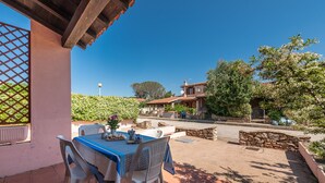 Un patio con una mesa y sillas, una pérgola y vistas a una zona residencial con árboles y una casa.