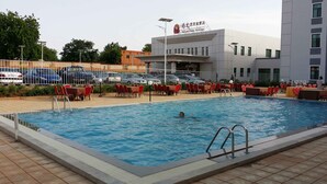 Ein Schwimmbecken mit einer darin schwimmenden Person, umgeben von roten Stühlen und Tischen, mit einem Hotel im Hintergrund.