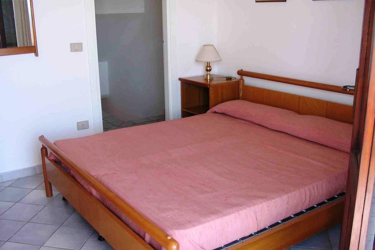 Une chambre à coucher avec un lit en bois, une table de chevet avec une lampe et une porte donnant sur une autre pièce.