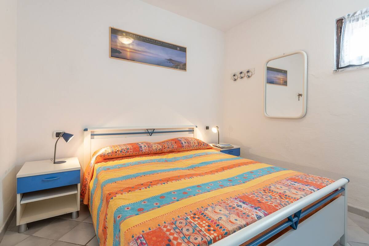 Une chambre à coucher avec un lit, une table de chevet, une lampe de chevet, un miroir et un tableau encadré accroché au mur.