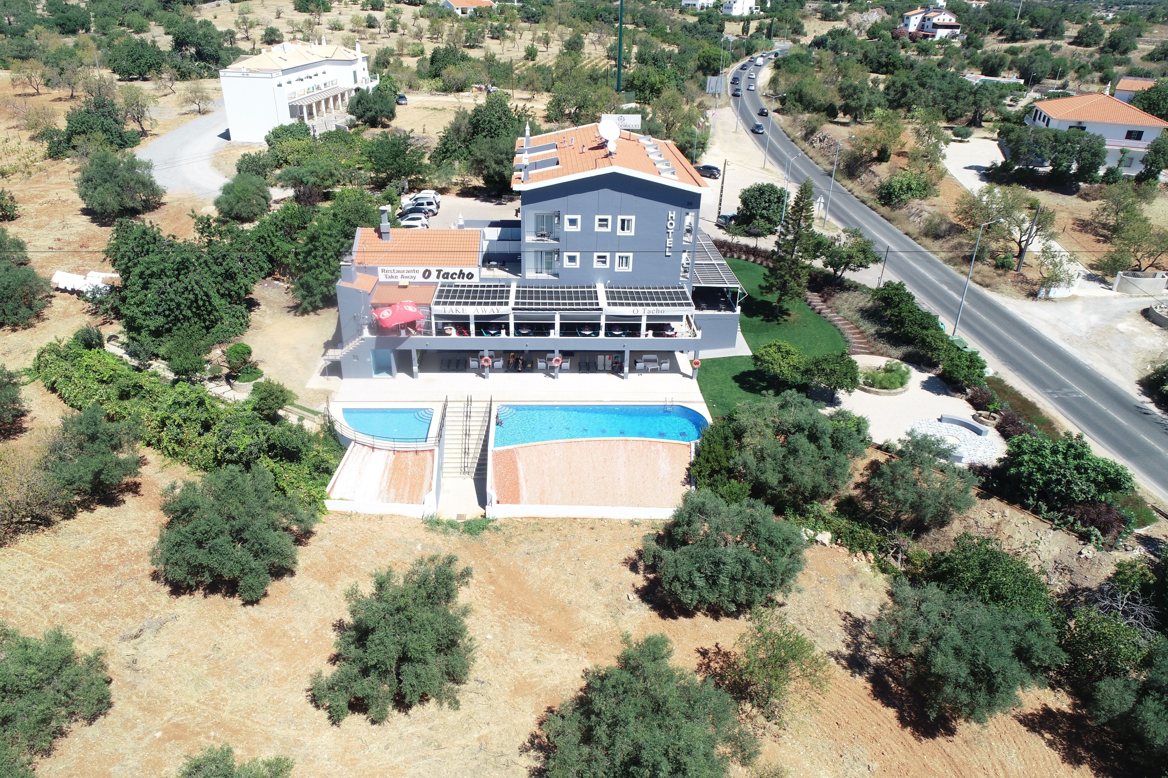 A two-story building with a swimming pool, a restaurant named 'Tacho', and a road nearby.