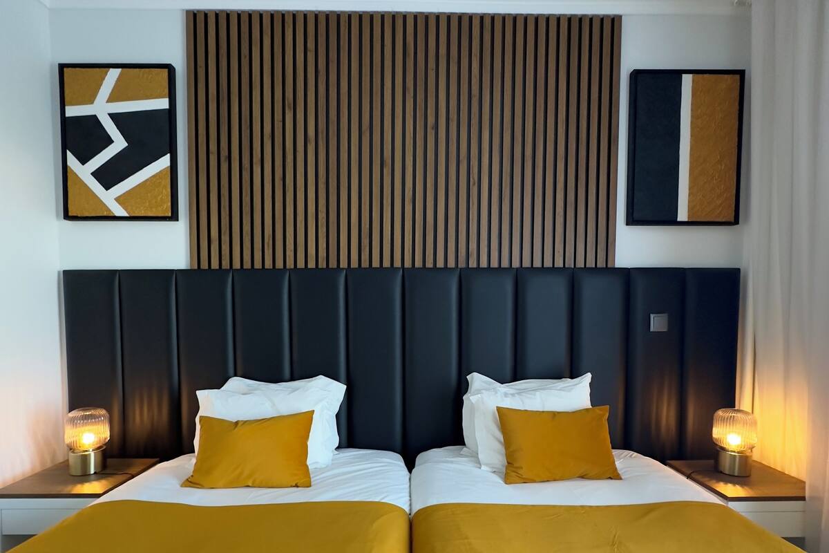 A hotel room with two beds, a wooden slat headboard, and two bedside lamps.