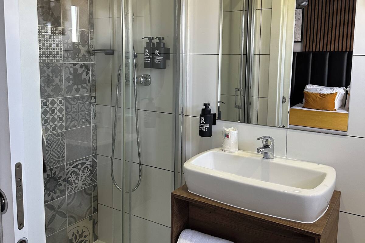 A modern bathroom with a glass-enclosed shower, a white sink, and a wooden vanity with towels.