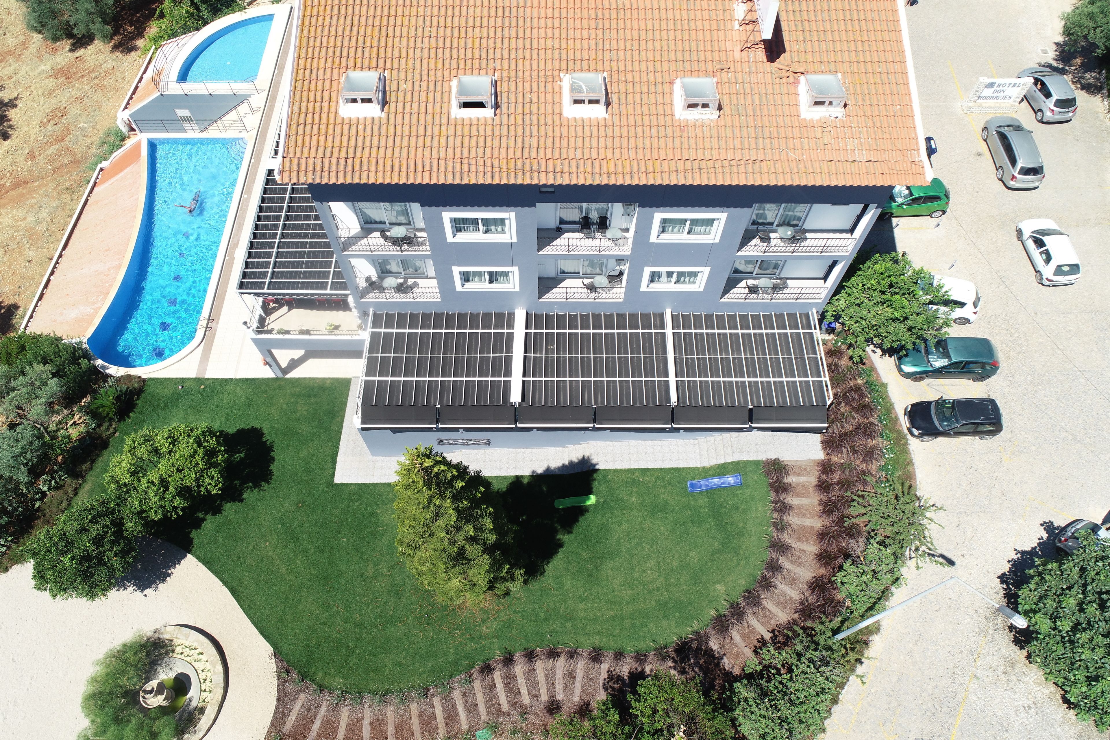 An aerial view of a building with a swimming pool, solar panels, and a parking lot.