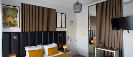 Une chambre d’hôtel moderne dotée d’un grand lit, de tables de chevet, d’un bureau, d’un miroir et d’un téléviseur à écran plat.