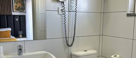 A modern bathroom with a white sink, toilet, and shower. There are towels on a shelf and a towel rack above the shower.