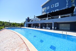 Una piscina con cubierta de azulejos azules, un edificio de hotel con un letrero que dice "O Tacho Restaurant Bike Andy" y un cielo despejado.