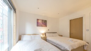 A hotel room with two beds, a wooden door, and a painting on the wall. - Piccadilly Gardens (Manchester)