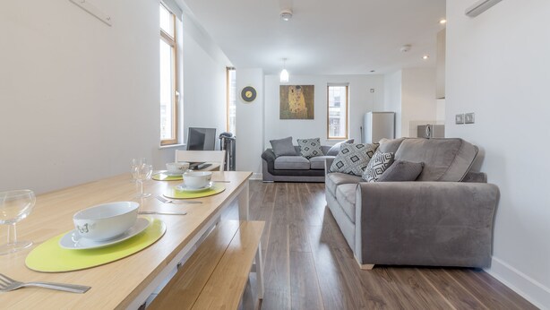 A modern living room with a grey sofa, a dining table with a yellow placemat, and a grey couch. - Piccadilly Gardens (Manchester)