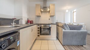 A compact kitchen with a built-in oven, a dishwasher, and a grey sofa in the adjacent living area. - Piccadilly Gardens (Manchester)
