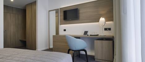 Habitación de hotel con cama, escritorio, silla, televisión y lámpara.