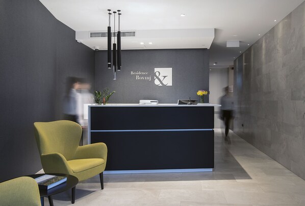 A modern reception area with a dark reception desk, a yellow armchair, and a black pendant light.