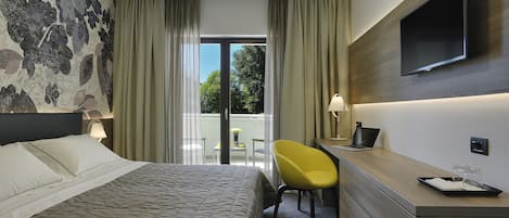 Hotelkamer met een bed, een bureau met stoel, een televisie en een balkon met uitzicht.