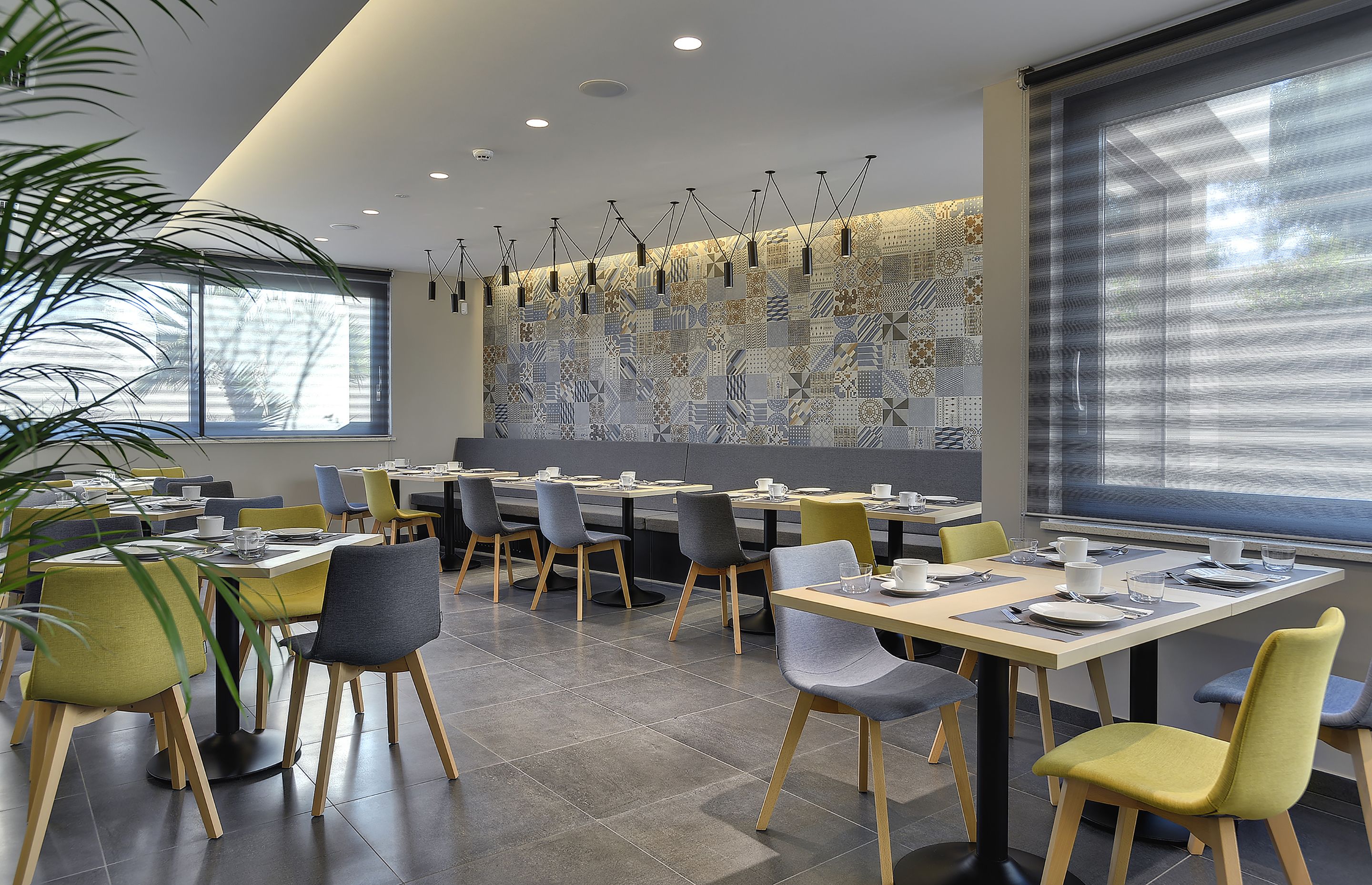 A modern dining area with multiple tables and chairs, large windows, and a decorative wall.