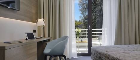 A hotel room with a bed, a desk with a laptop, a chair, and a TV mounted on the wall.