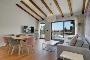 A modern living room with a wooden ceiling, a dining area with chairs, a sofa, and a TV.