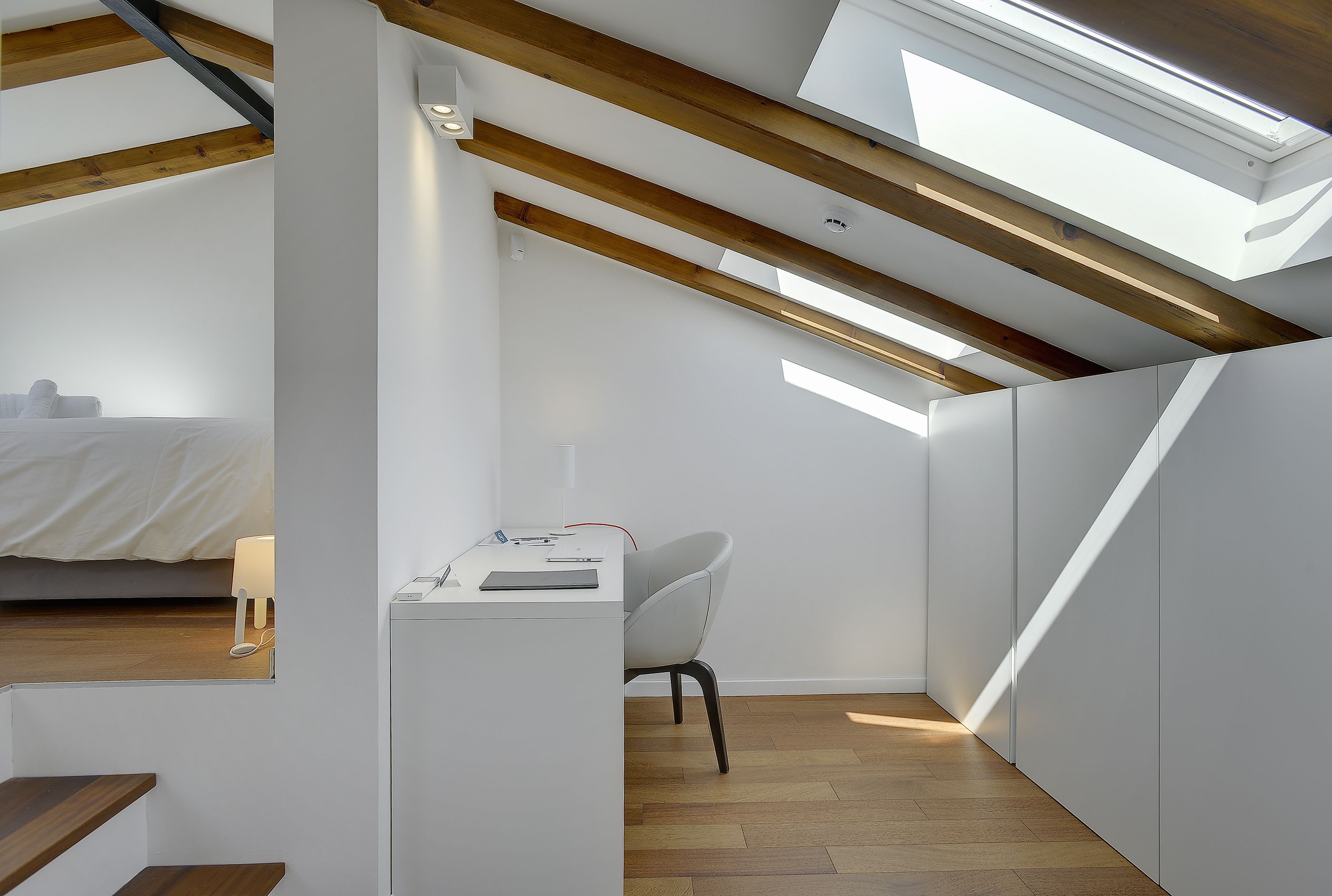 Un dormitorio moderno y luminoso en ático, con tragaluces, un escritorio y una silla.