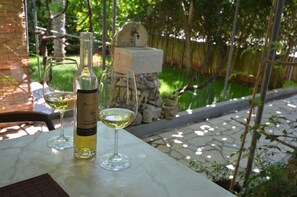 A table with two wine glasses and a bottle, set outdoors with a stone wall and greenery in the background.