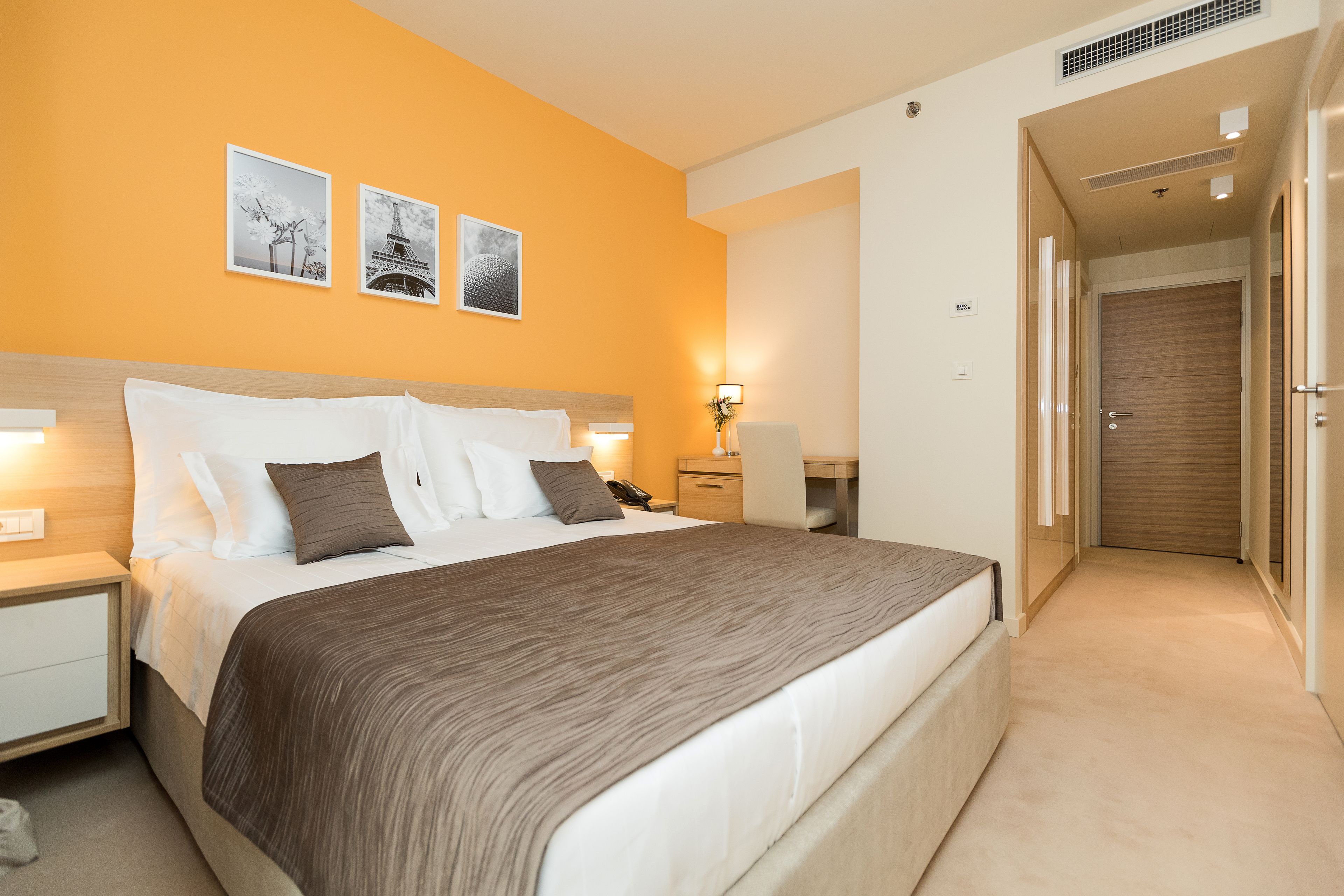 A hotel room with a large bed, bedside tables, a desk, and a wardrobe.