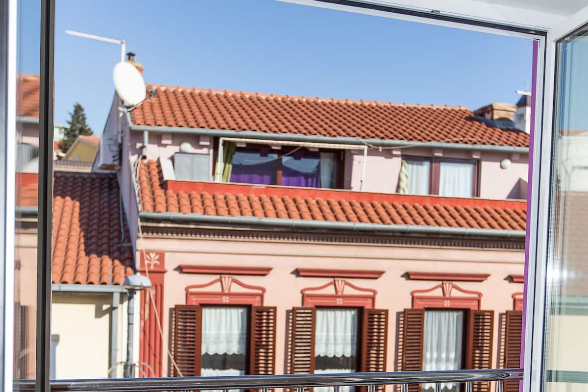 Een balkon met metalen hekwerk met uitzicht op een gebouw met rode dakpannen en roze muren.