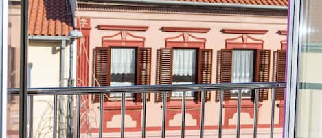 Un balcón con barandillas metálicas que da a un edificio con tejados rojos y paredes rosadas.