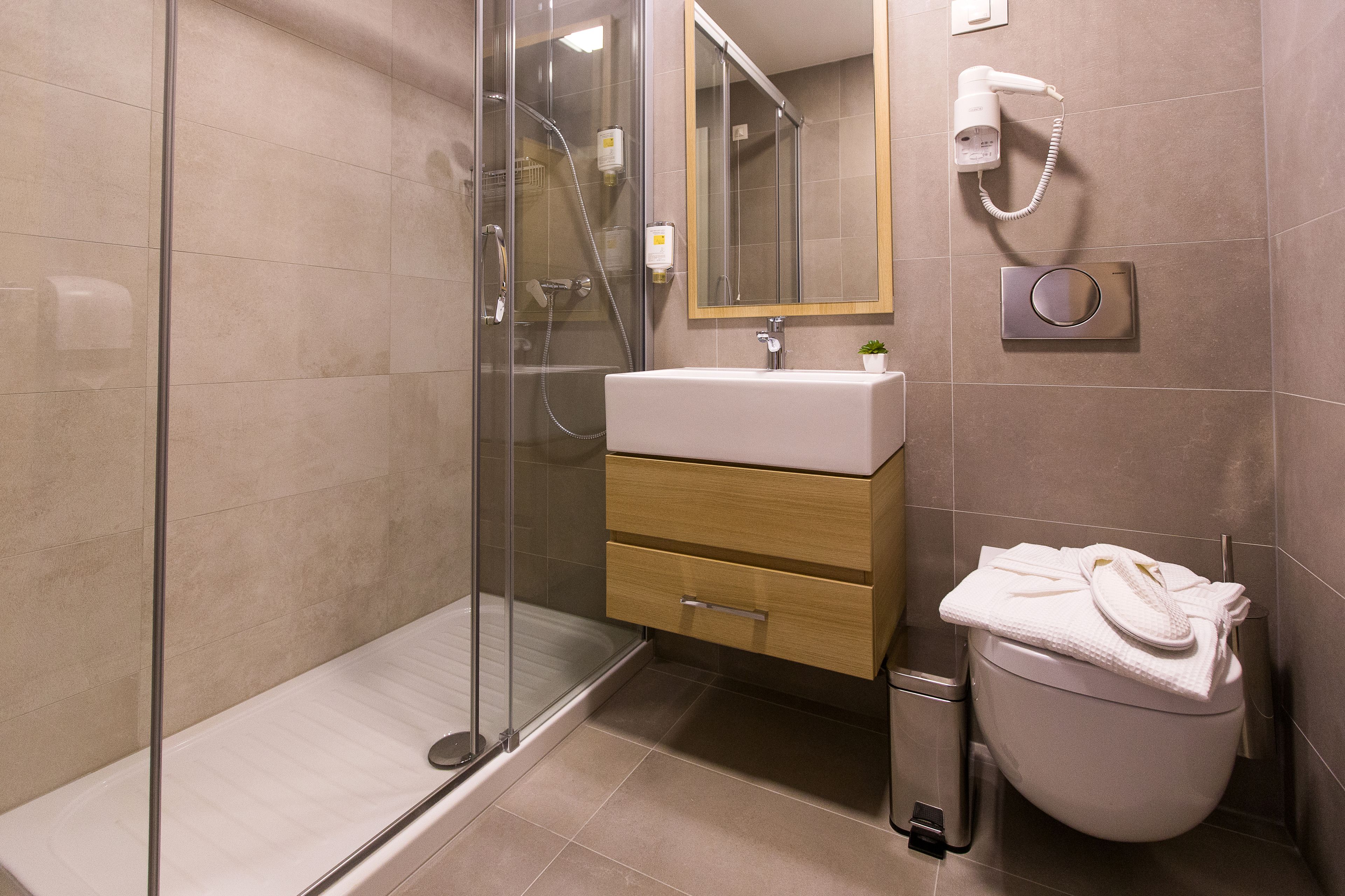 Ein modernes Badezimmer mit Duschkabine aus Glas, Waschbecken mit Spiegel darüber und Toilette mit Handtuchhalter.