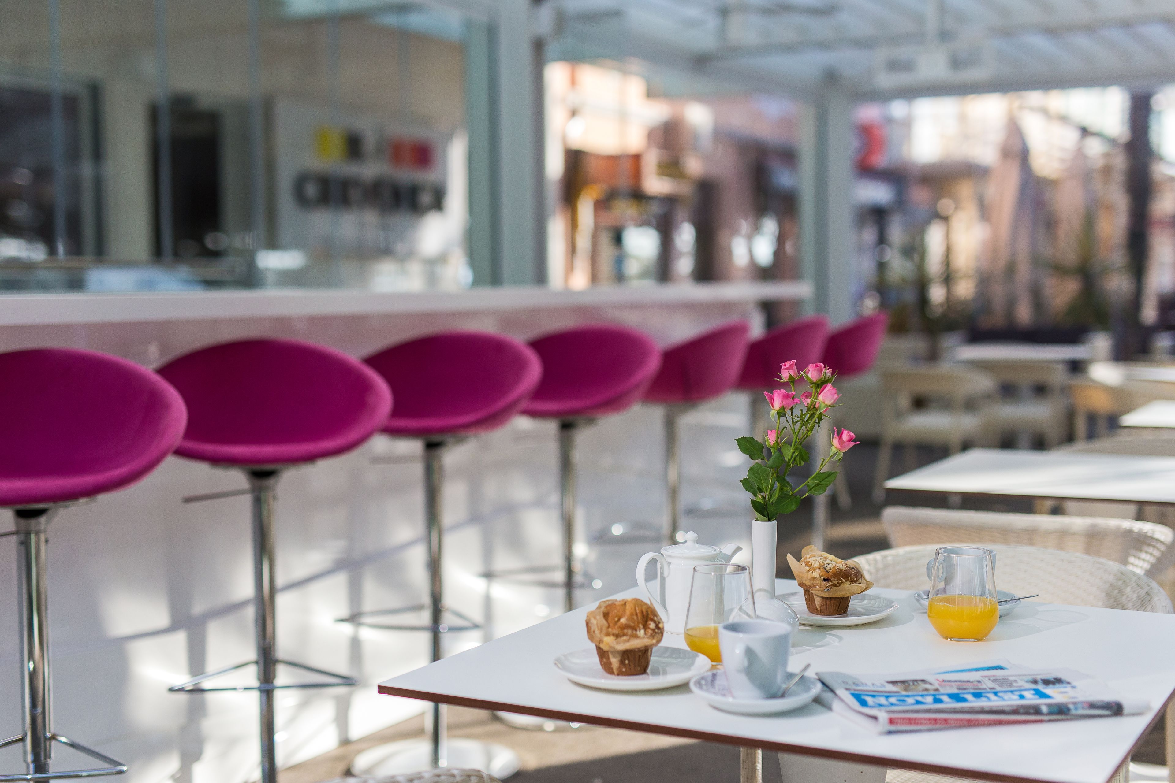 A cafe with pink chairs, a table with a muffin, a pitcher, and a glass of orange juice.