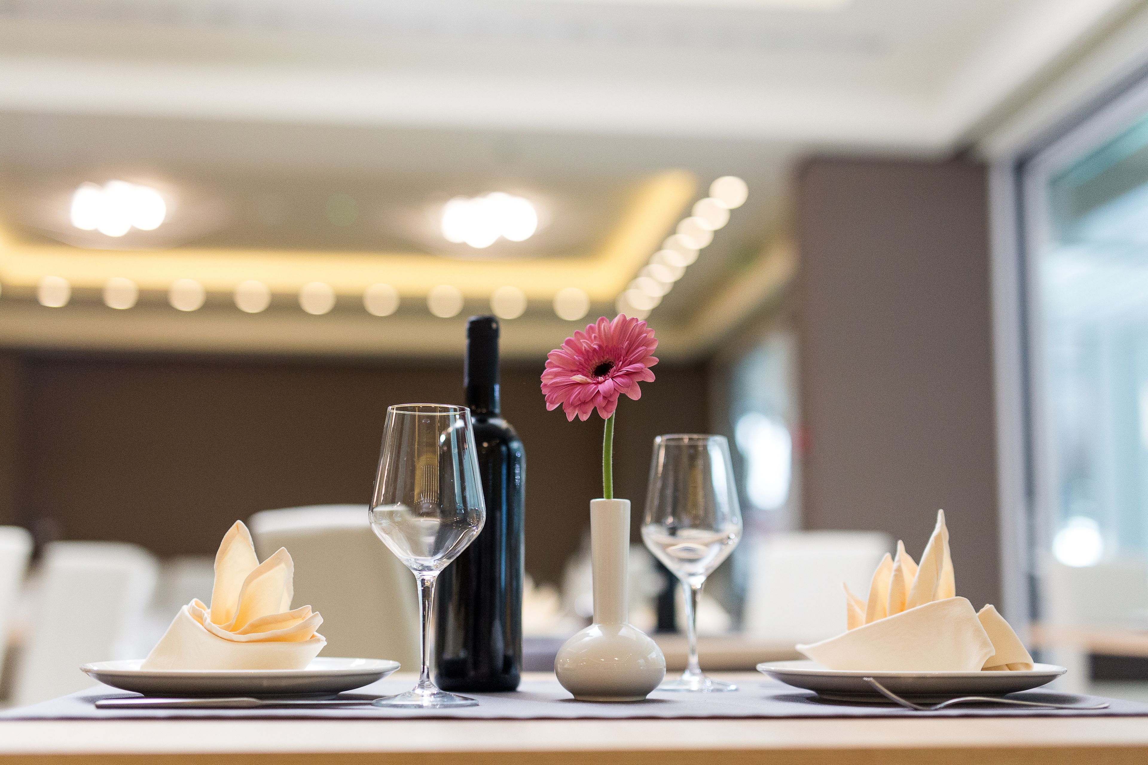 A dining table with a vase, a bottle, and a flower.