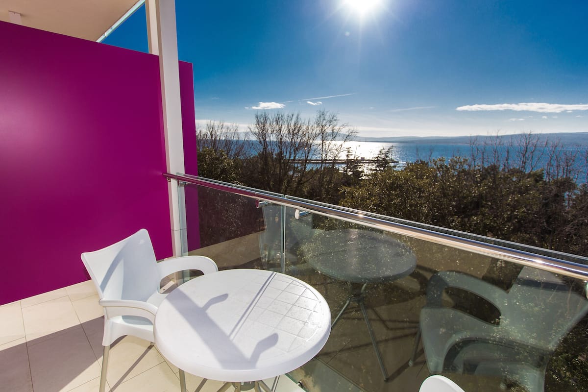 Een balkon met glazen hekwerk, witte stoelen en een tafel.