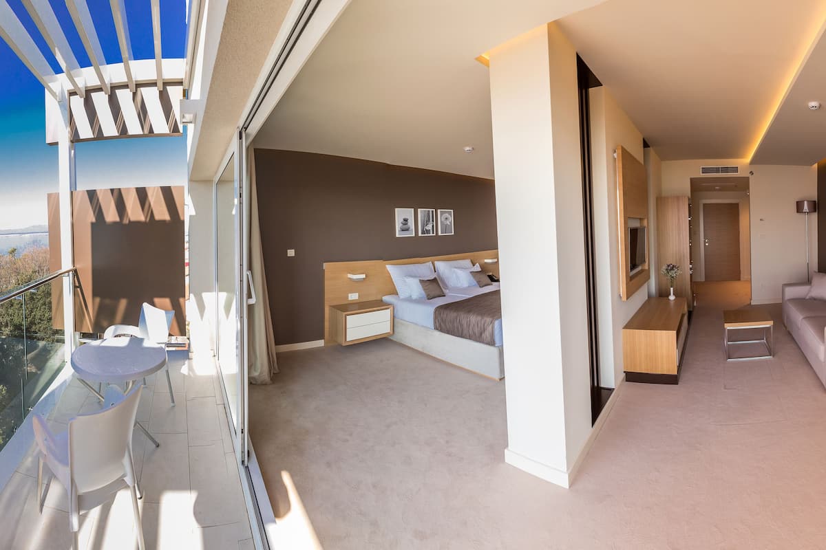 Een moderne slaapkamer met een groot bed, een zithoek met een bank en een bijzettafeltje, en een balkon met een glazen deur.