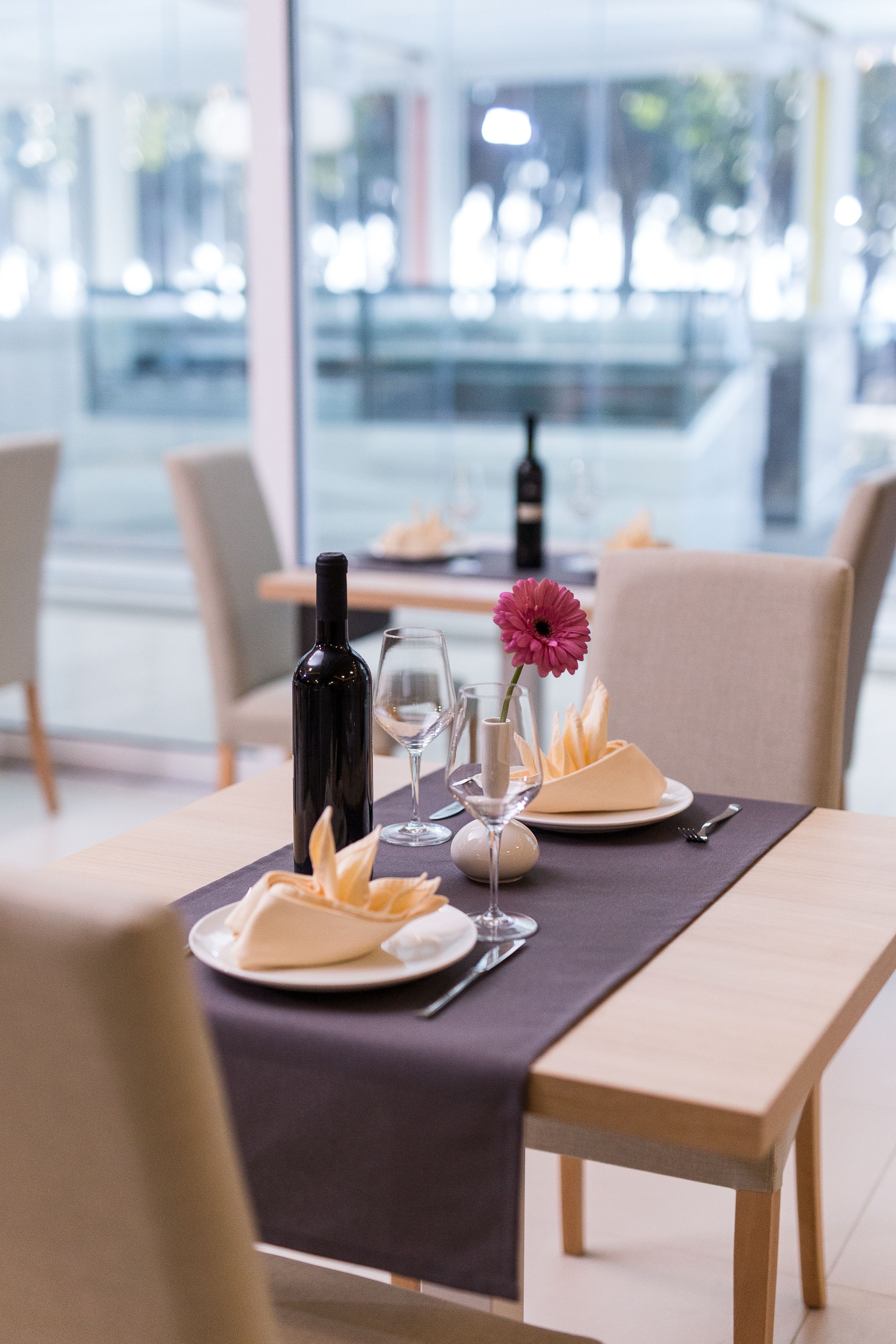 A dining table set with a bottle, wine glass, and a flower arrangement.