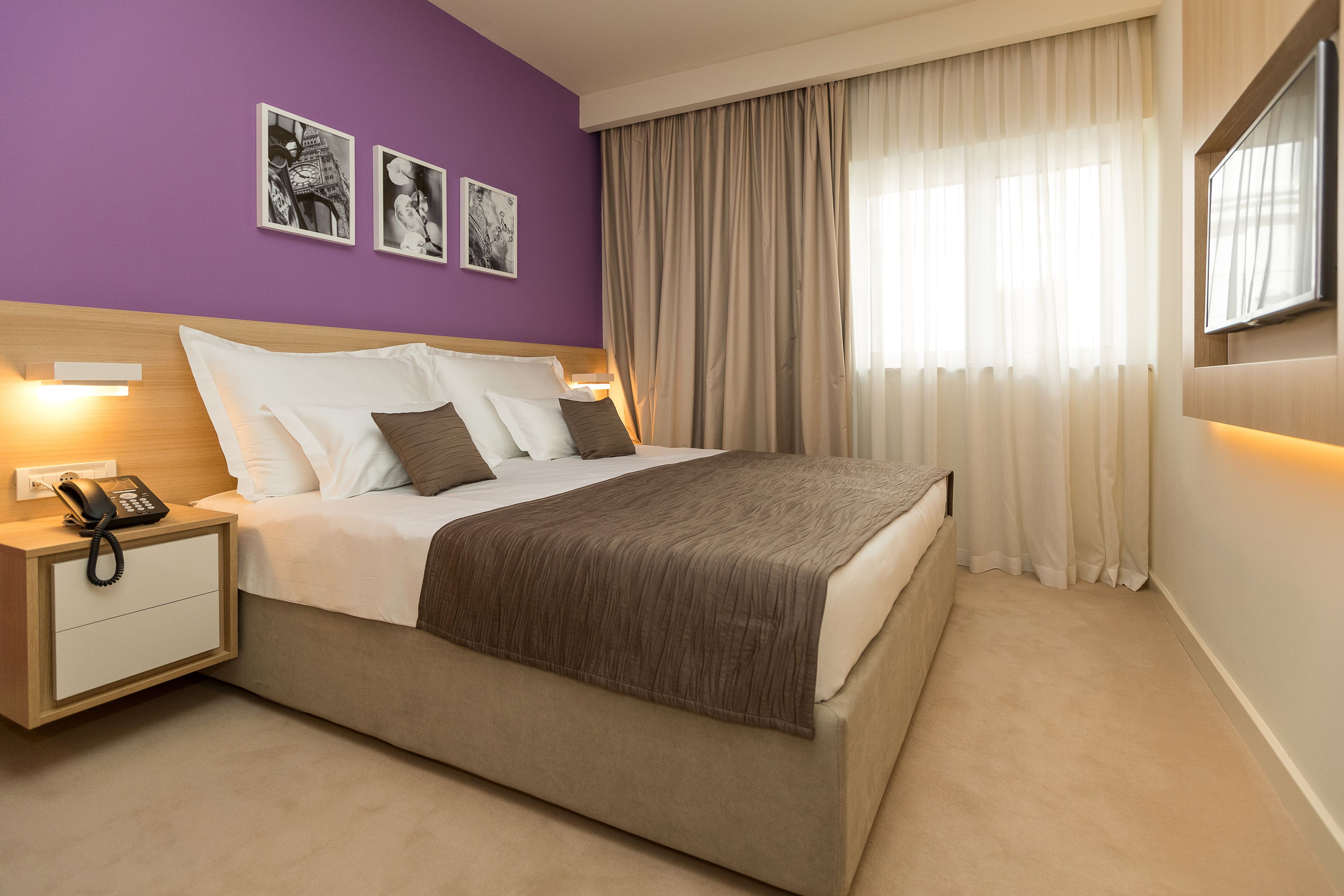 Una habitación de hotel con cama, mesitas de noche, teléfono y una obra de arte en la pared.
