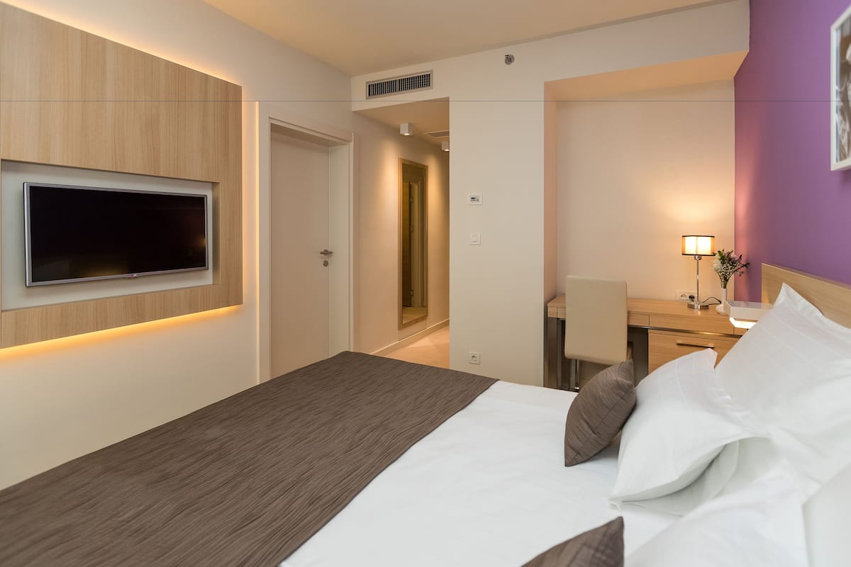 Een hotelkamer met een bed, een bureau, een stoel, een aan de muur bevestigde televisie en een lamp.