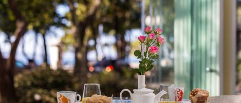 A table with a white pitcher, a cup with a coffee logo, a muffin, a glass of orange juice, and a vase with pink flowers.