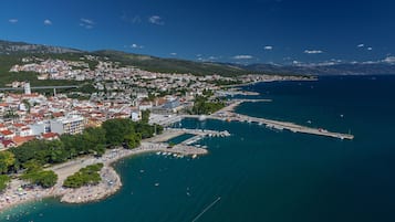 An aerial view of a coastal town with a marina, beach, and mountainous backdrop.