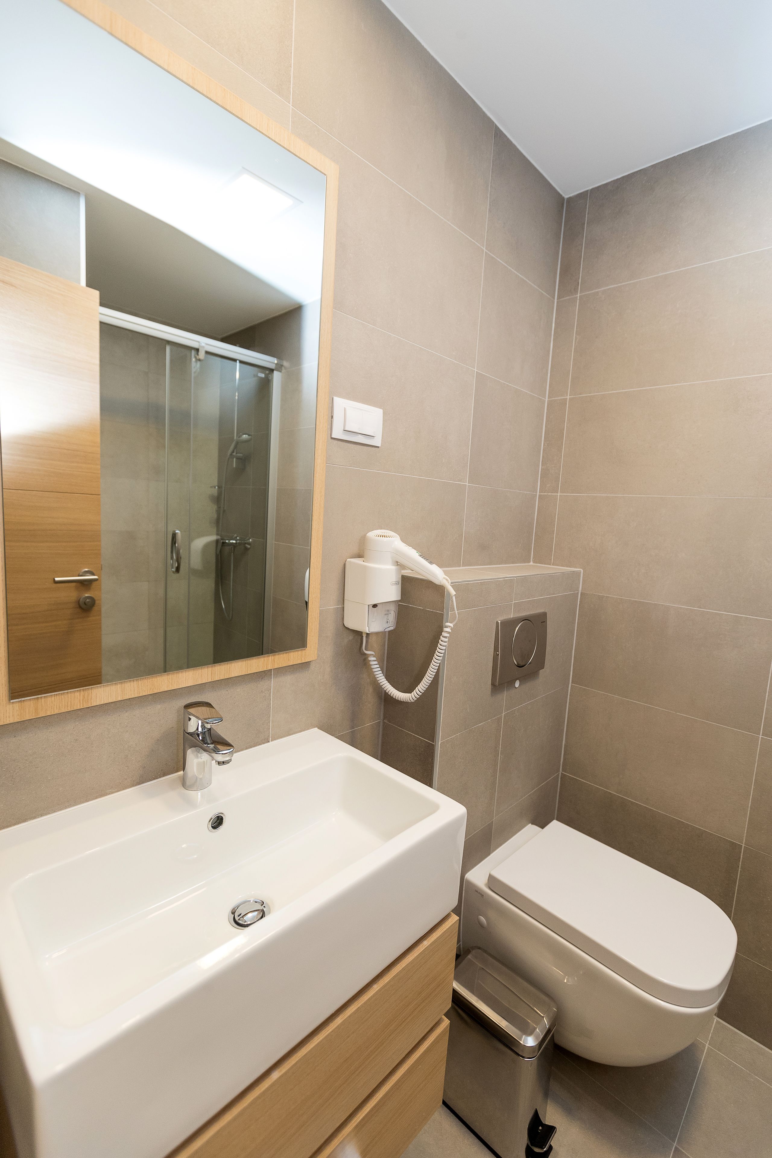 Un baño moderno con lavamanos, espejo y retrete blancos.
