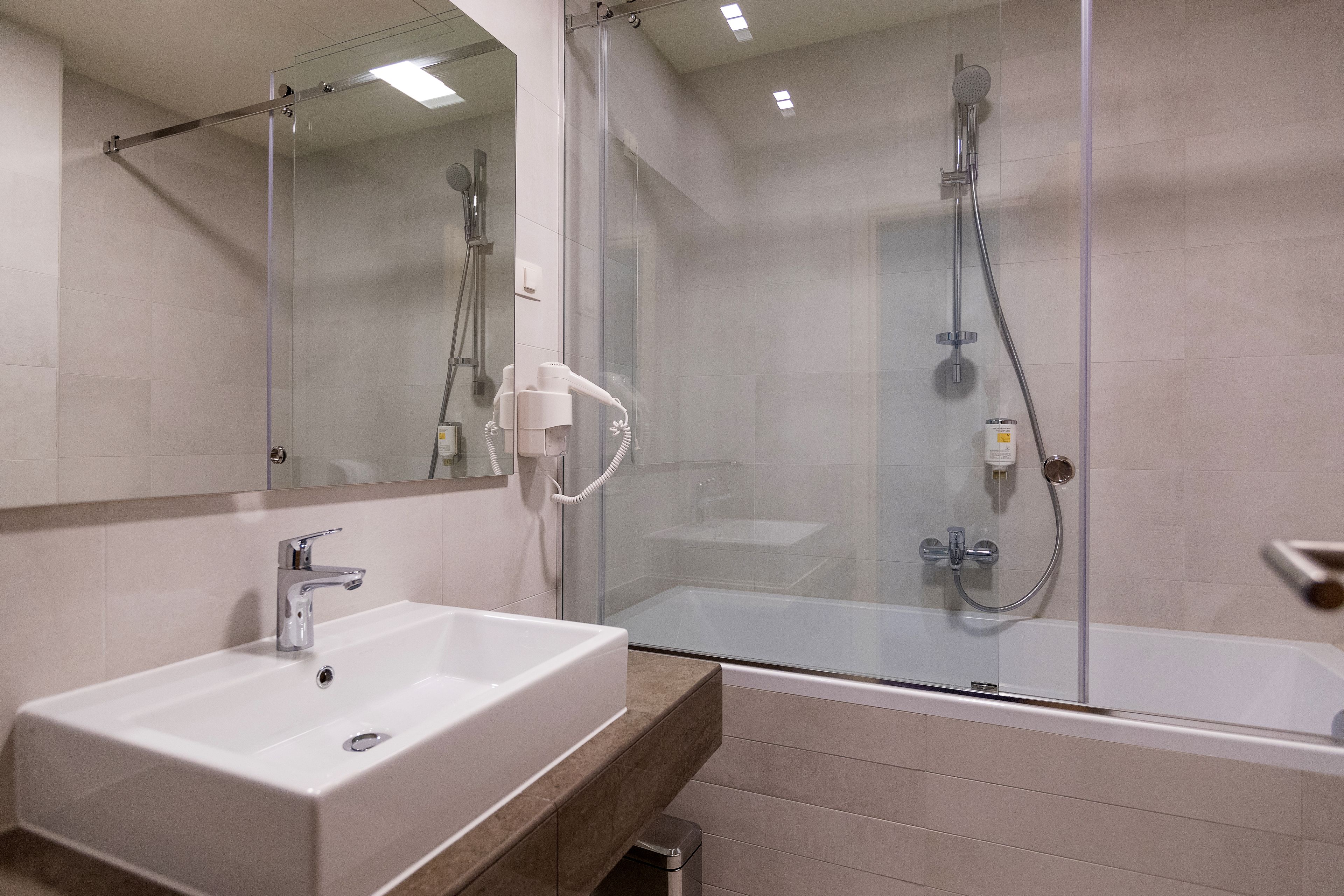 Un baño moderno con ducha envuelta en cristal, un lavamanos con espejo y una bañera.