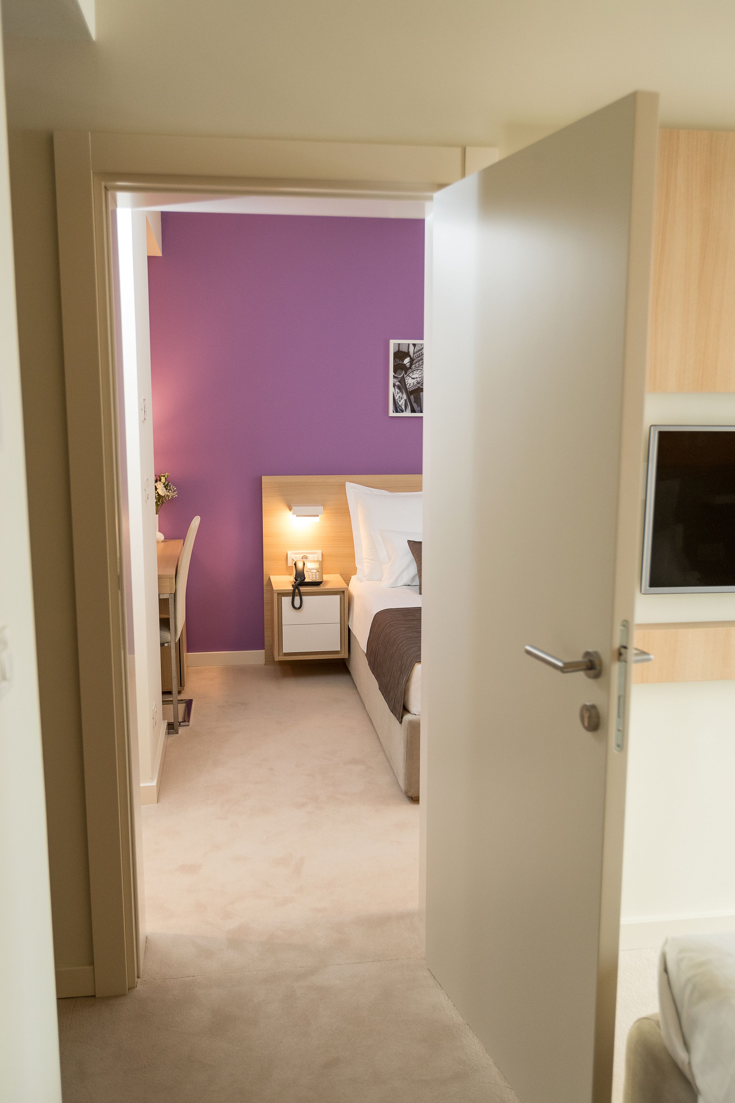 A hotel room with a bed, bedside table, lamp, and a television on the wall.