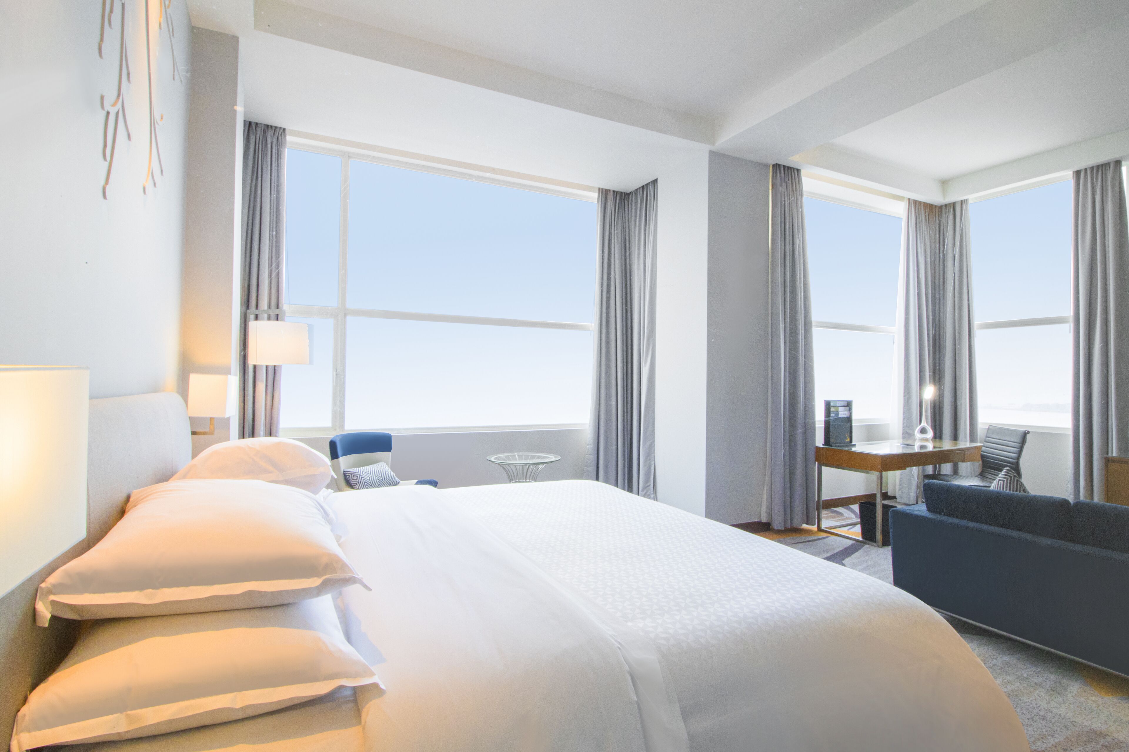 A hotel room with a large bed, a desk, a chair, and a sofa.