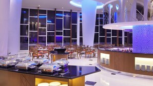 Un moderno vestíbulo de hotel con zona de buffet, arreglos de asientos y un amplio ventanal con vistas a la ciudad.