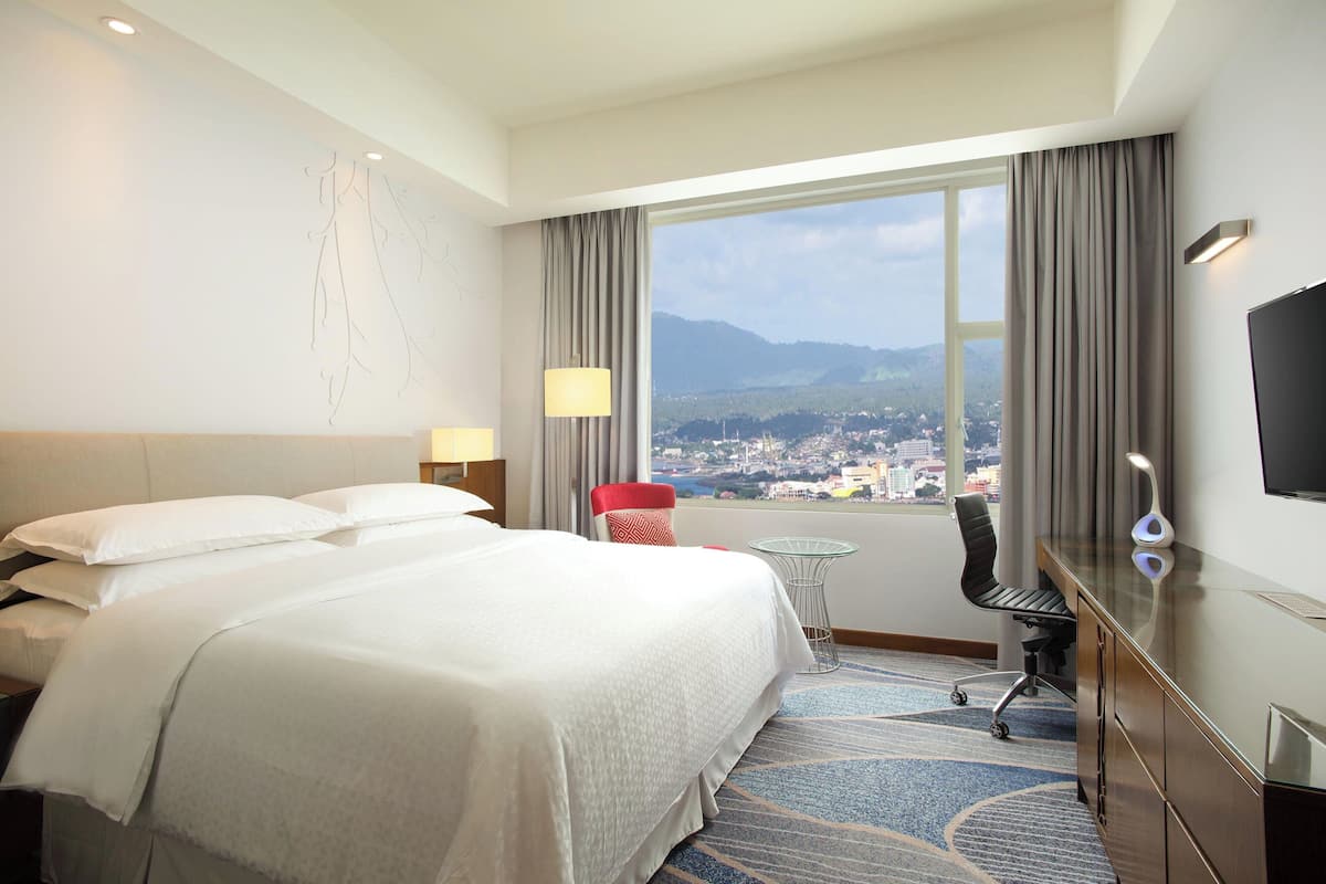 A hotel room with a large bed, a desk, a chair, a small table, and a TV.