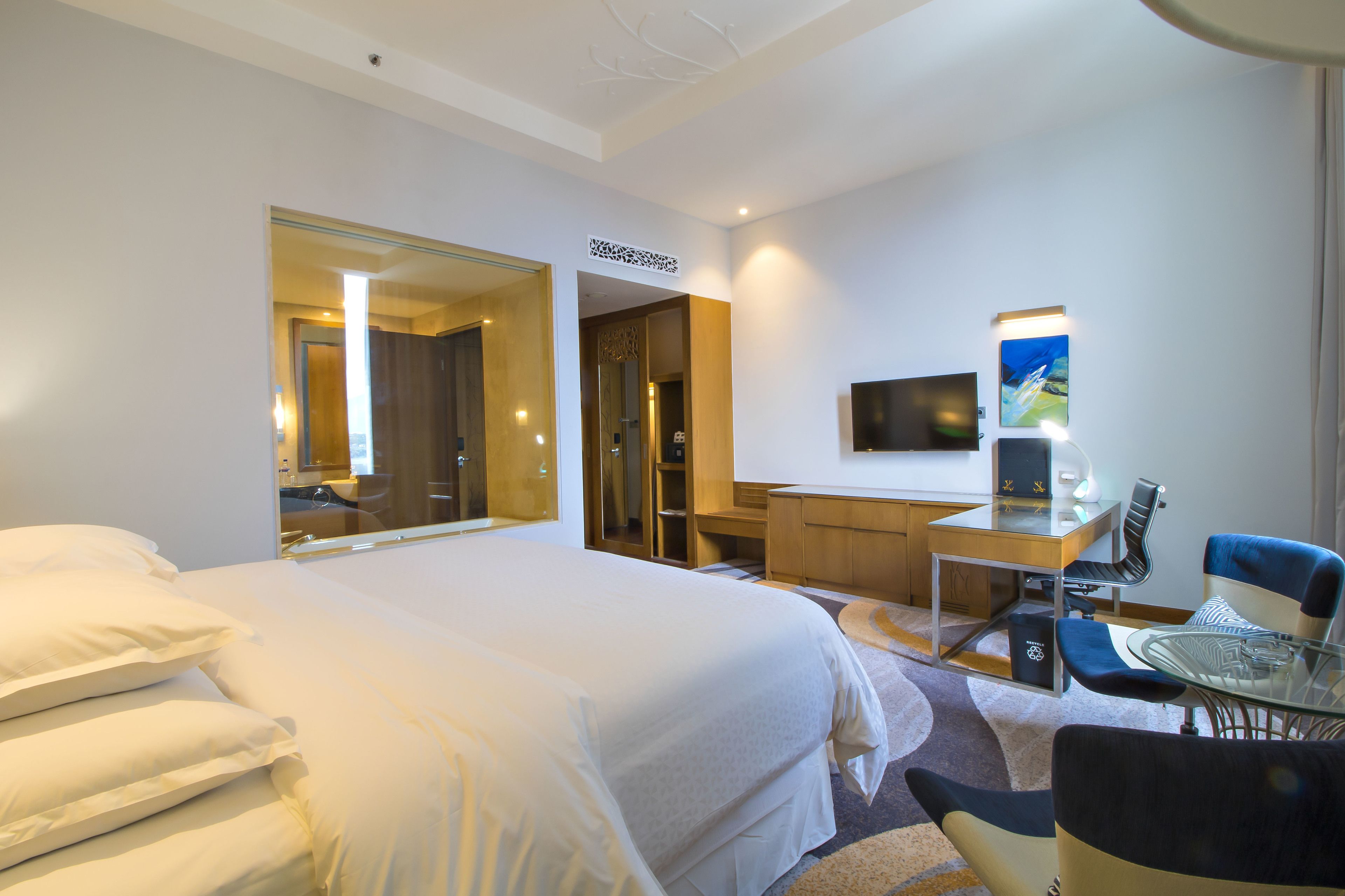 A hotel room with a large bed, a desk with a chair, a TV, and a mirror.