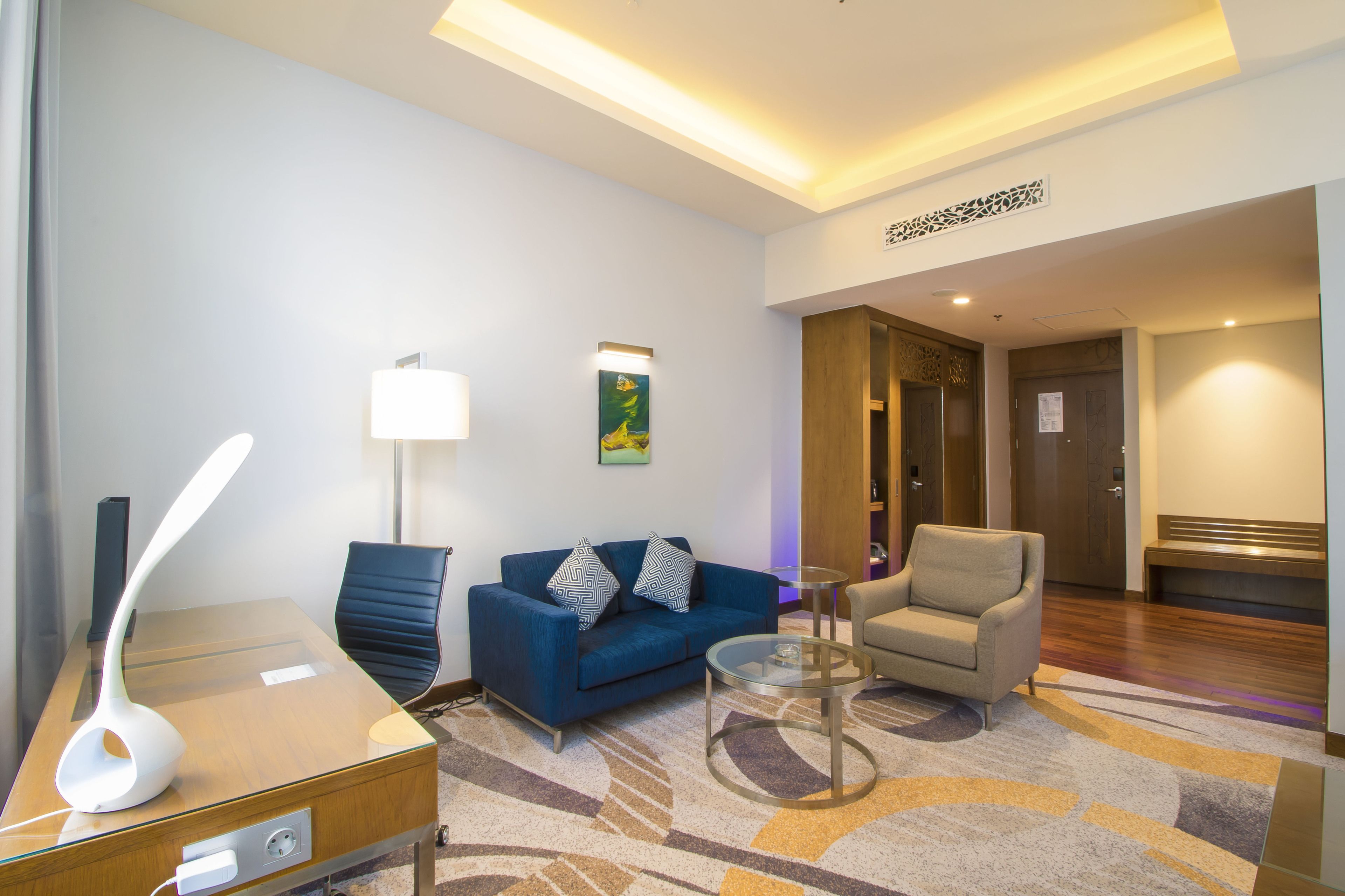 A modern hotel lobby with a blue sofa, a round coffee table, a lamp, and a bench.