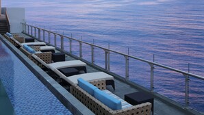 Zona junto a la piscina con sillones de descanso y vista al océano.