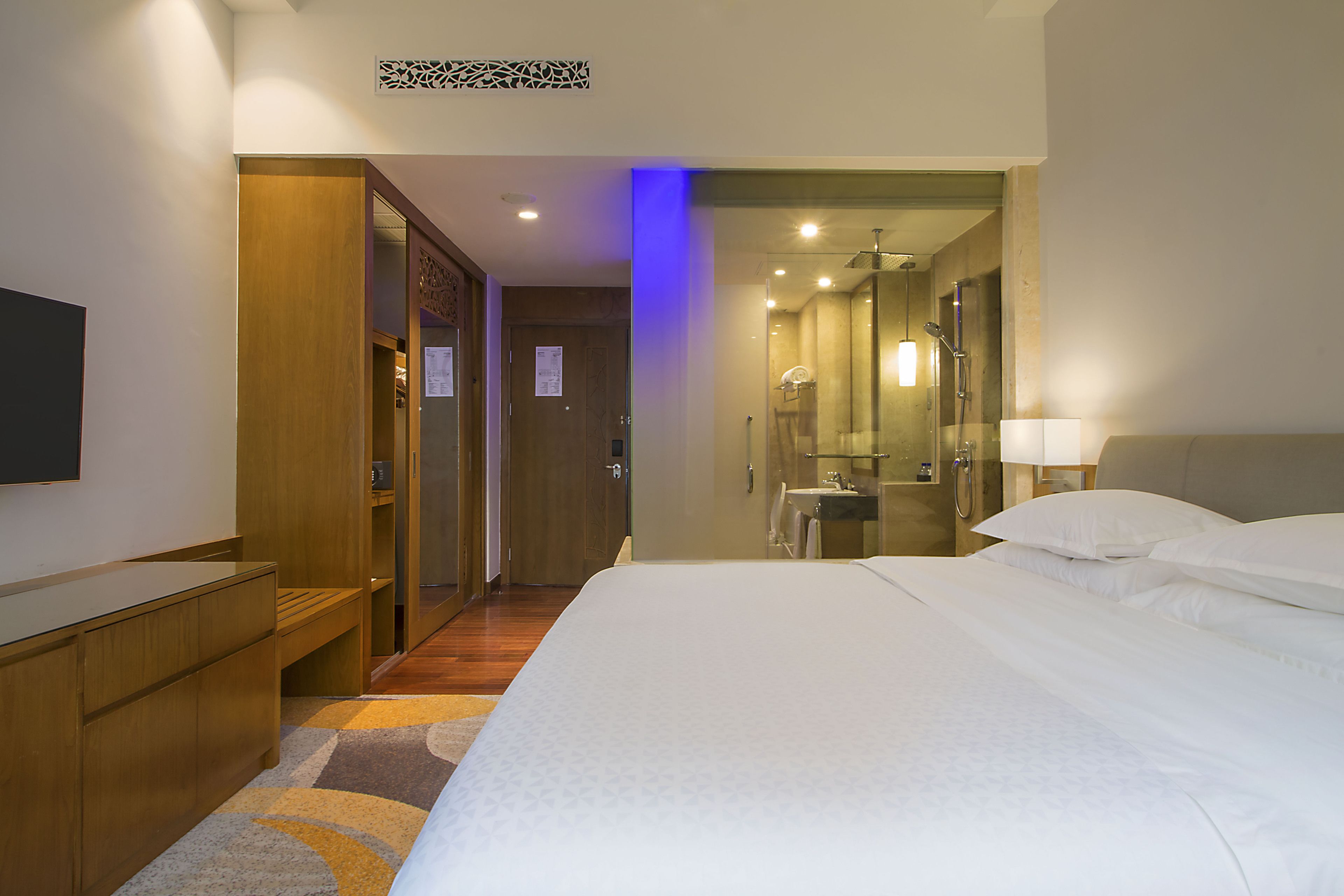 A hotel room with a bed, a desk, a mirror, and a shower area.