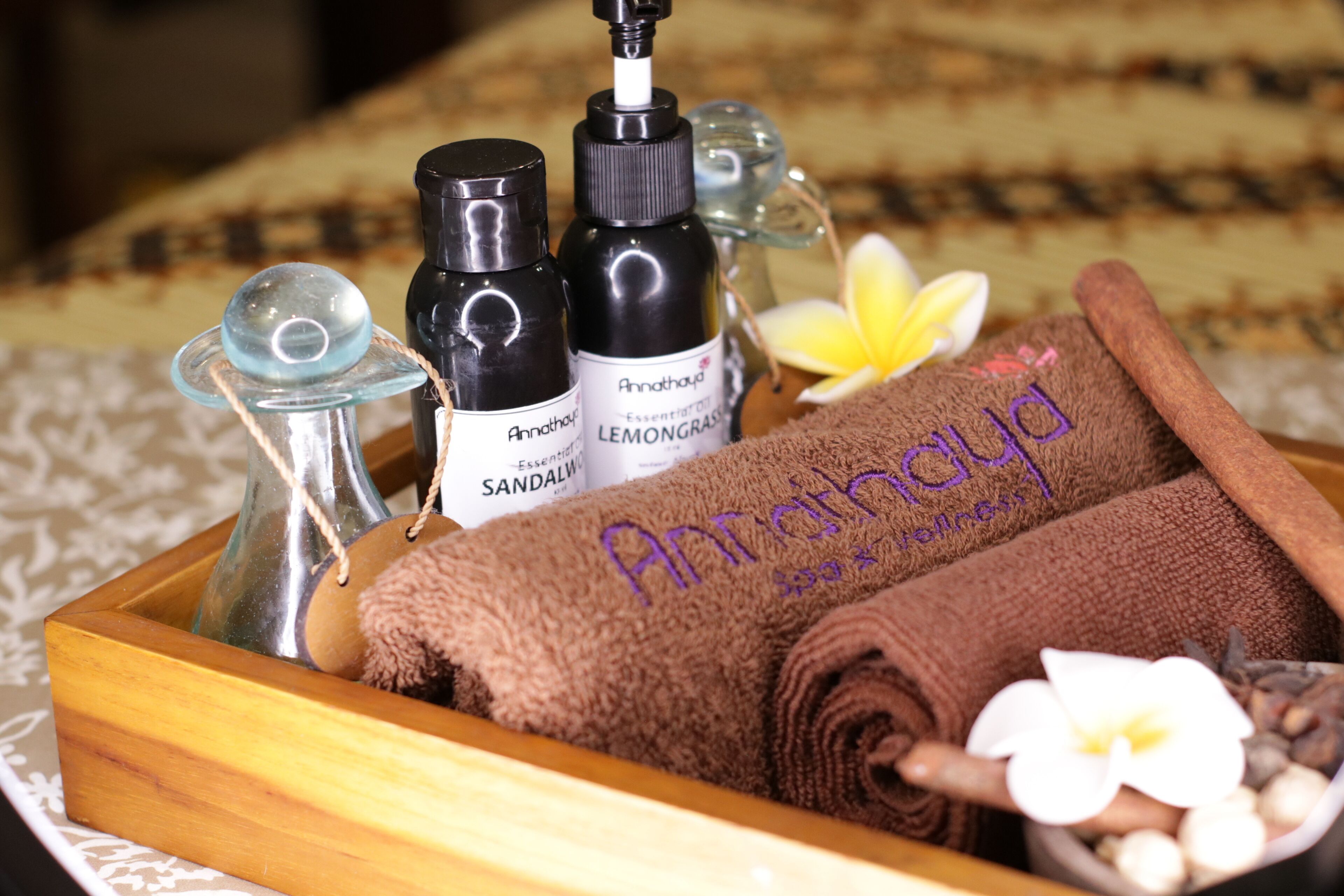 A wooden tray with a brown towel, bottles of essential oils, and a glass container.