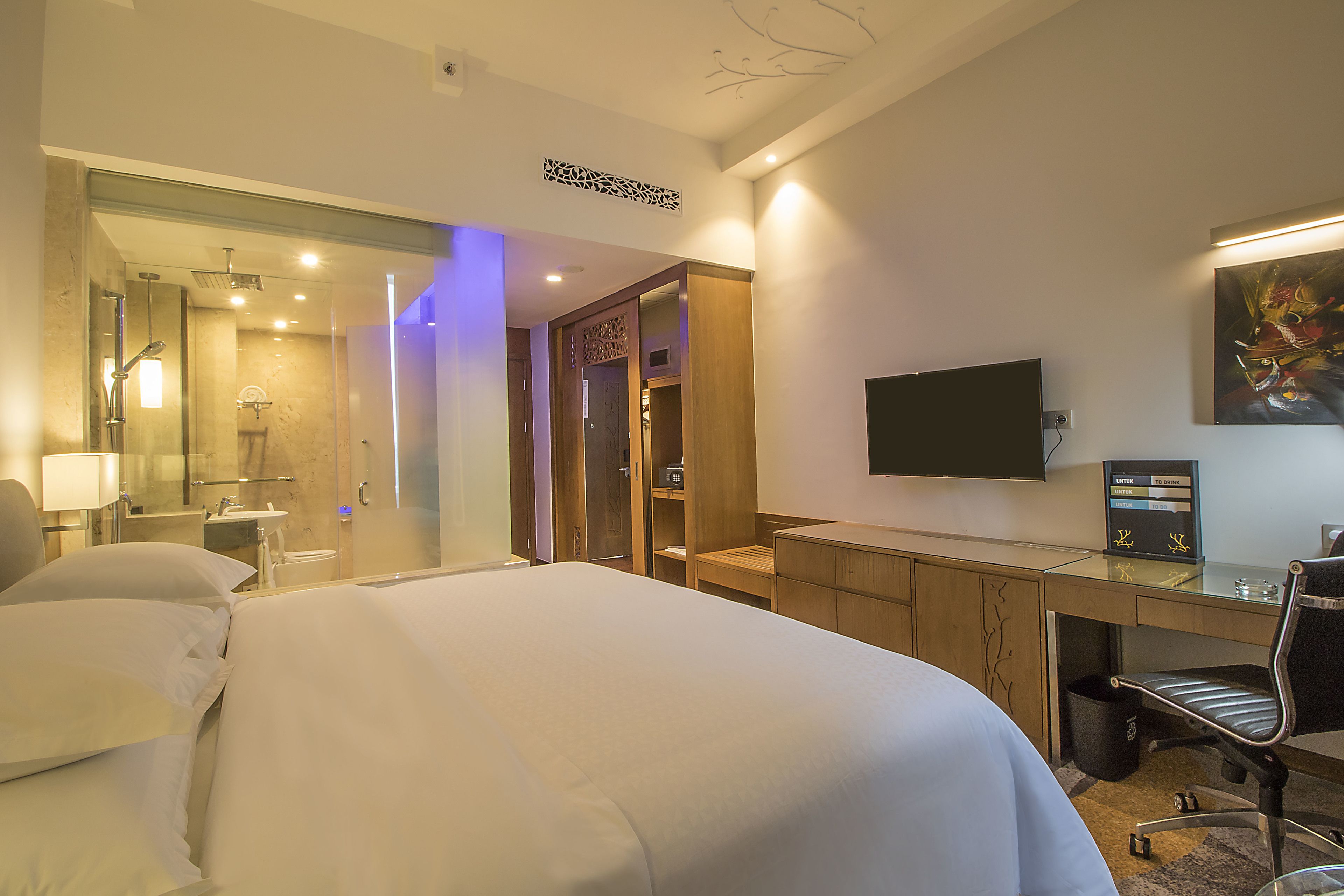 Habitación de hotel con una cama grande, un escritorio con silla, televisión y baño con ducha y espejo.