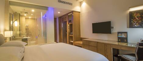 Habitación de hotel con una cama grande, un escritorio con silla, televisión y baño con ducha y espejo.