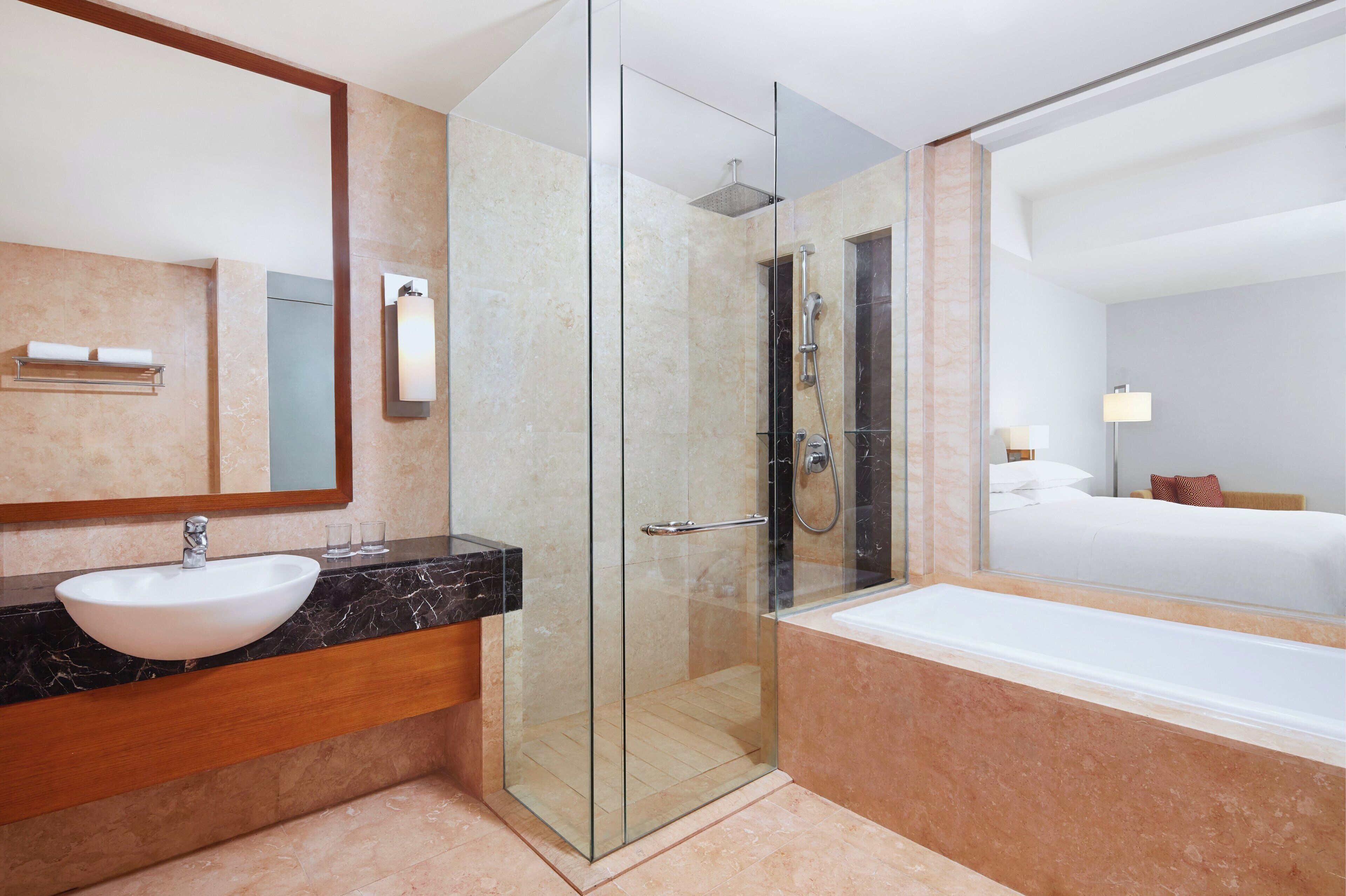A modern hotel bathroom with a glass-enclosed shower, a marble sink, and a large mirror.